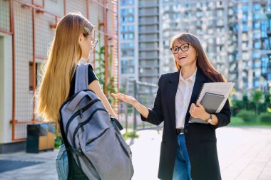 Orta yaşlı bayan öğretmen, akıl hocası, koç, yönetmen, sosyal hizmet görevlisi açık havada genç kız öğrencilerle konuşuyor, eğitim binası geçmişi var. Eğitim, öğrenme, gençlik, yaş lise konsepti