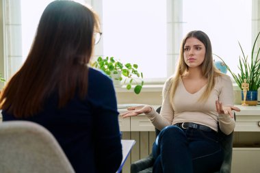 Üzgün, mutsuz, depresyondaki genç bir kadın hasta, kadın psikiyatrist psikologla terapide. Psikoloji, psikoterapi, tedavi yardım desteği, gençlik akıl sağlığı konsepti