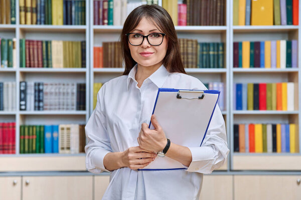 Portrait serious woman with clipboard inside library office classroom, middle aged female teacher mentor coach, psychologist therapist counselor. Professional educational, mental specialist, people