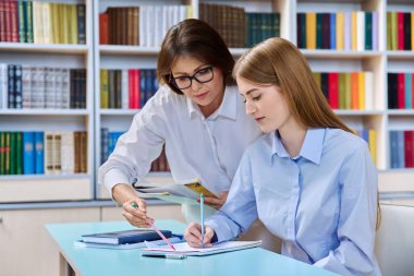 Genç kız öğrenci kütüphane raflarıyla birlikte sınıfın içinde bayan öğretmen eğitmen eğitmeniyle çalışıyor. Eğitim, ergenlik, lise, üniversite, bilgi, öğrenim kavramı