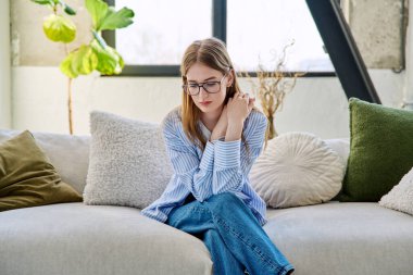Üzgün, mutsuz, genç bir kadın evinde, kanepede oturuyor. Gençlik sağlığı, üzüntü, sorunlar depresyon, acı kavramı