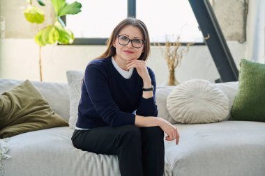 Orta yaşlı, güzel bir kadının portresi. Kanepede oturuyor. Gözlüklü, çekici, olgun bir kadın. Güzellik, sağlık, yaşam tarzı, insan kavramı