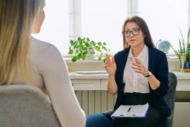 Orta yaşlı kadın psikoterapist genç bir kadınla seans terapisi ruh sağlığı uzmanı sosyal hizmet görevlisi olarak çalışıyor. Not panosuna not alıyor. Psikoterapi psikoloji danışmanlık desteği