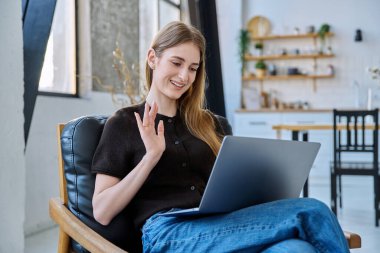 Genç ve güzel bir kadın internette sohbet konferansı için dizüstü bilgisayar kullanıyor. Evde, sandalyesinde oturuyor. İletişim öğrenmek için dijital teknolojiler boş zamanlarında sosyal medya bloglarında çalışır