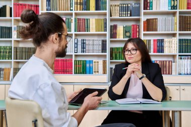 Orta yaşlı kadın ruh sağlığı uzmanı. Genç erkek hastayla çalışıyor. Ofiste birlikte oturuyorlar. Terapi, psikoloji, psikoterapi, danışmanlık, profesyonel destek konsepti