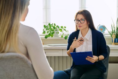 Orta yaşlı kadın psikoterapist genç bir kadınla seans terapisi ruh sağlığı uzmanı sosyal hizmet görevlisi olarak çalışıyor. Not panosuna not alıyor. Psikoterapi psikoloji danışmanlık desteği