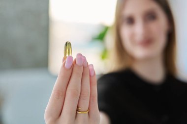Genç bir kadının elindeki sarı omega-3 balık yağı kapsülünü kapatın. Sağlıklı beslenme, diyet, vitaminler, gıda takviyeleri, sağlık hizmetleri kavramı