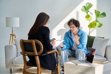 Zihinsel terapi seansında gülümseyen genç erkek hasta uzman psikolog psikoterapist danışman sosyal hizmet görevlisiyle konuşuyor. Hizmet psikolojisi psikoterapi desteği