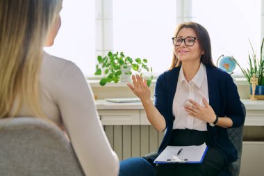 Orta yaşlı kadın psikoterapist genç bir kadınla seans terapisi ruh sağlığı uzmanı sosyal hizmet görevlisi olarak çalışıyor. Not panosuna not alıyor. Psikoterapi psikoloji danışmanlık desteği