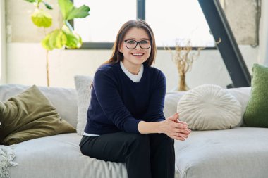 Orta yaşlı, güzel bir kadının portresi. Kanepede oturuyor. Gözlüklü, çekici, olgun bir kadın. Güzellik, sağlık, yaşam tarzı, insan kavramı