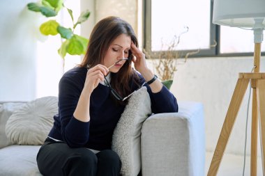 Olgun, üzgün, stresli bir kadın. Stresli, zihinsel ve fiziksel bir acı yaşıyor. Kanepede oturuyor. Sorunlar yalnızlık, baş ağrısı hormon stresi, orta yaşlı kadınların sağlığı