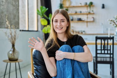 Genç ve güzel bir kadının portresi, gülümseyen üniversite öğrencisi evinde oturan kameraya bakıyor. Çekici kadın sarışın, yaşam tarzı, gençlik kavramı.