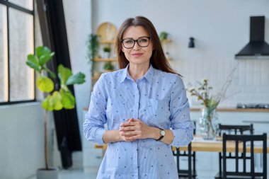 Kendinden emin, orta yaşlı, güzel bir kadın. Kameraya bakıyor. Evin içinde. Başarı, güven, yaşam tarzı, olgun insanlar konsepti