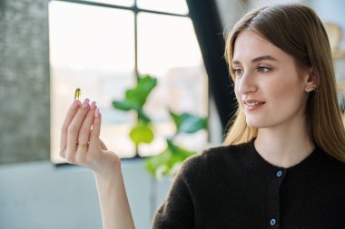 Genç, güzel, gülümseyen bir kadın balık yağı Omega 3 ile sarı kapsül hapı alıyor, evde duruyor. Sağlıklı beslenme, diyet, vitaminler, gıda takviyeleri, sağlık hizmetleri kavramı
