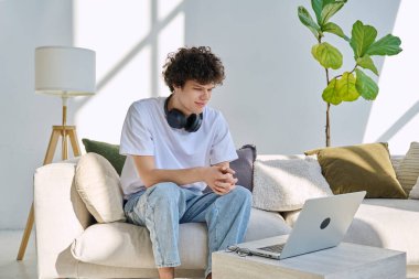 Evdeki kanepede oturmuş dizüstü bilgisayara bakan yakışıklı adam. Boş zamanlarında çalışma iletişim teknolojileri, yaşam tarzı, gençlik kavramı