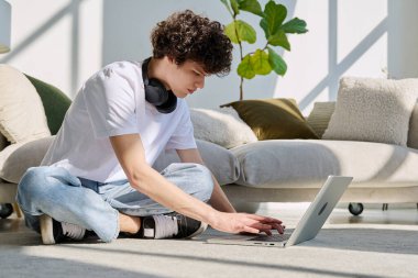 Evdeki kanepenin yanında dizüstü bilgisayarda yazan yakışıklı bir erkek portresi. Kıvırcık, güler yüzlü, 20 yaşında bir öğrenci. Yaşam tarzı, eğitim, teknoloji, gençlik kavramı