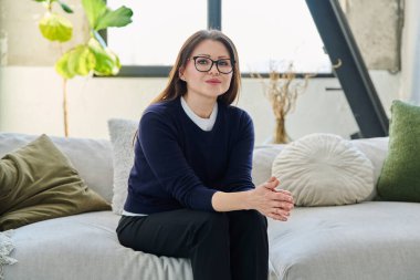 Orta yaşlı, güzel bir kadının portresi. Kanepede oturuyor. Gözlüklü, çekici, olgun bir kadın. Güzellik, sağlık, yaşam tarzı, insan kavramı