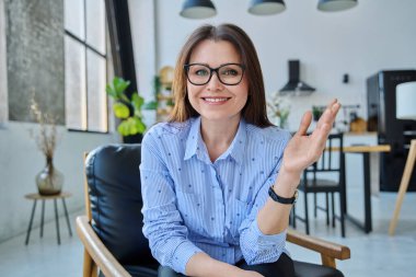 Orta yaşlı, kendine güveni tam başarılı bir kadın, web kamerasına bakıyor, video konferans görüşmesi yapıyor, ofisteki koltukta oturuyor. Sanal sohbet uzaktan toplantı oturumu kayıt vlog teknolojisi iş dünyası