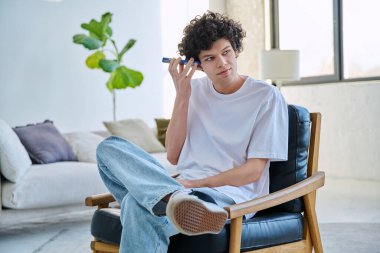 Genç adam akıllı telefondan sesli mesaj dinliyor, kulağının yanında telefonu tutan gülümseyen adam, evinde koltukta oturuyor.