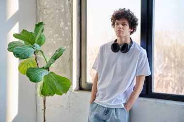 Kulaklıklı, pencerenin yanında, fotokopi odası olan yakışıklı bir adam. Havalı kıvırcık saç stili olan poz veren adam başka tarafa bakıyor. Gençlik, yaşam tarzı, yirmili yaşlar konsepti