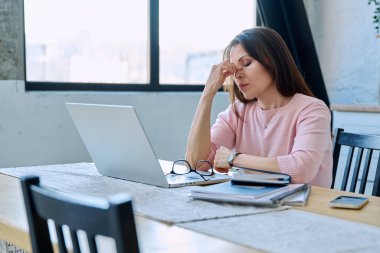 Depresyonda olan, stresli, zihinsel ve fiziksel acı çeken olgun bir kadın bilgisayar laptopuyla masada oturuyor. Sorunlar yalnızlık, baş ağrısı hormon stresi, orta yaşlı kadınların sağlığı