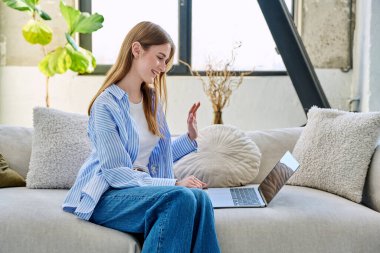 Genç ve güzel bir kadın internette sohbet etmek için dizüstü bilgisayar kullanıyor. Evde, kanepede oturuyor. İletişim öğrenmek için dijital teknolojiler boş zamanlarında sosyal medya bloglarında çalışır