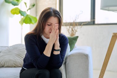 Olgun, üzgün, stresli bir kadın. Stresli, zihinsel ve fiziksel bir acı yaşıyor. Kanepede oturuyor. Sorunlar yalnızlık, baş ağrısı hormon stresi, orta yaşlı kadınların sağlığı