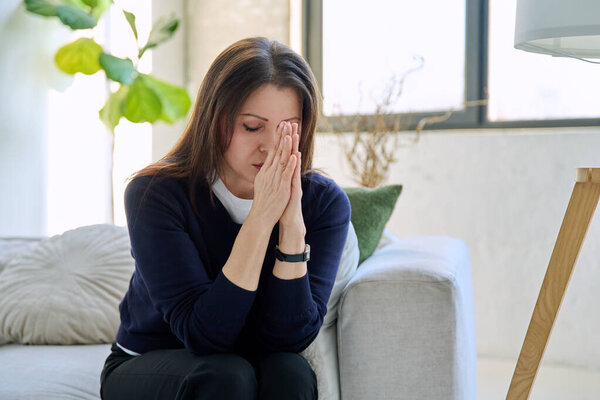 Mature sad depressed stressed woman experiencing stress, mental and physical pain sitting at home on sofa couch. Problems difficulties loneliness, headache hormonal stress, health of middle-aged women