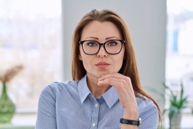 Ofisinde mavi gömlekli, kendine güvenen, orta yaşlı, zarif bir iş kadınının portresi. Güzellik, iş, kariyer, başarı, iş, olgun yaş insanları kavramı