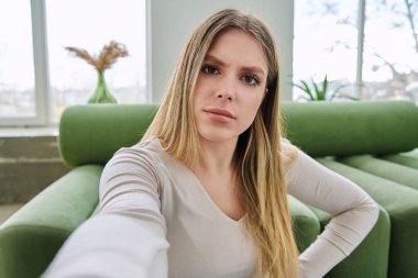 Özçekim portresi. Evinde çok güzel bir genç kadın var. Kafası karışmış, 20 'li yaşlarda, uzun sarı saçlı, kameraya bakan çekici bir kadının yüzünü kapatın. Gençlik, yaşam tarzı konsepti