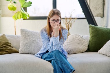 Üzgün, mutsuz, genç bir kadın evinde, kanepede oturuyor. Gençlik sağlığı, üzüntü, sorunlar depresyon, acı kavramı