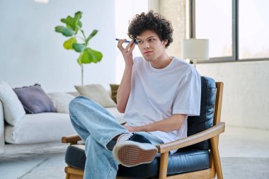 Genç adam akıllı telefondan sesli mesaj dinliyor, kulağının yanında telefonu tutan gülümseyen adam, evinde koltukta oturuyor.