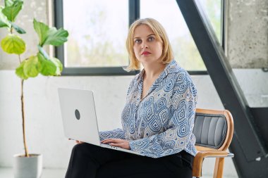 Ciddi orta yaşlı bir iş kadını dizüstü bilgisayarla koltukta oturuyor ve kameraya bakıyor. Teknoloji, iş, iş, 40 'lı yılların insan kavramı