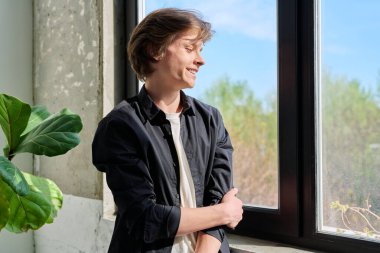 Pencereden dışarı bakan yakışıklı genç adam. Olumlu genç adam, profil görüşü. Ergenlik, yaşam tarzı, 16-17 yaş arası gençler.