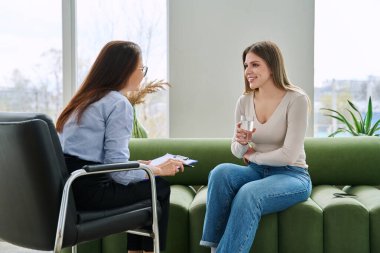 Bireysel terapi seansında kadın psikolog sosyal danışman ile konuşan genç bir kadın uzman ofisinde kanepede yan yana oturuyor. Psikoloji danışmanı zihinsel yardım desteği