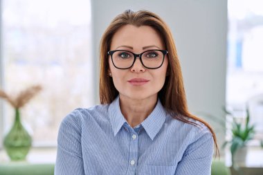 Ofisinde mavi gömlekli, kendine güvenen, orta yaşlı, zarif bir iş kadınının portresi. Güzellik, iş, kariyer, başarı, iş, olgun yaş insanları kavramı