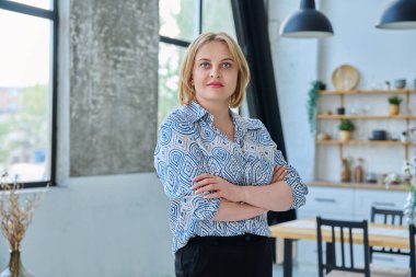 Ev içinde kollarını kavuşturmuş, kendinden emin, orta yaşlı güzel bir kadının portresi. Sarı saçlı, mavi gözlü, kameraya bakan 40 'larında gülümseyen bir kadın. Güzellik, sağlık, yaşam tarzı konsepti