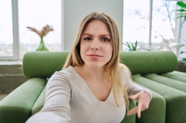 Özçekim portresi. Evinde çok güzel bir genç kadın var. Kafası karışmış, 20 'li yaşlarda, uzun sarı saçlı, kameraya bakan çekici bir kadının yüzünü kapatın. Gençlik, yaşam tarzı konsepti