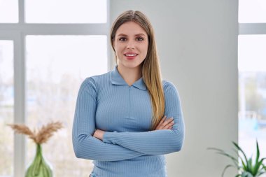 İç mekanda kollarını kavuşturarak poz veren kendinden emin genç bir kadının portresi. Gülümseyen mutlu 20 'li yaşlarda, sarışın, uzun saçlı, kameraya bakan bir kadın. Güzellik sağlık yaşam tarzı gençlik kavramı