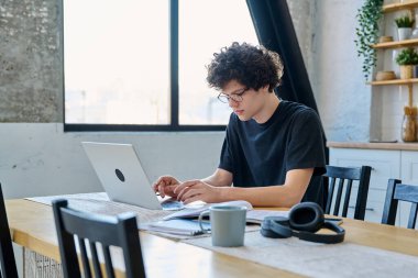 Ciddi bir üniversite öğrencisi dizüstü bilgisayarda yazı yazıyor, evde masada oturuyor. Yakışıklı kıvırcık erkek uzaktan çalışıyor, sınavlara hazırlanıyor. Teknoloji eğitimi dili öğrenme gençliği