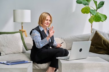 Orta yaşlı iş kadını evdeki kanepede oturan dizüstü bilgisayarla görüntülü konuşma görüşmesi yapıyor. Uzaktan görüşme, iş görüşmesi, online terapi oturumu, iş tele-teknoloji konsepti.