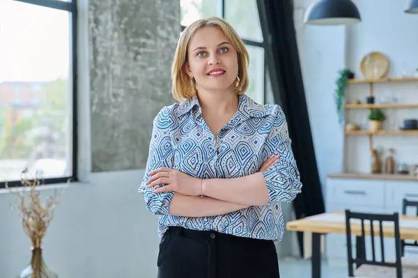 Ev içinde kollarını kavuşturmuş, kendinden emin, orta yaşlı güzel bir kadının portresi. Sarı saçlı, mavi gözlü, kameraya bakan 40 'larında gülümseyen bir kadın. Güzellik, sağlık, yaşam tarzı konsepti