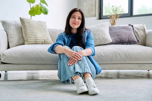 Oturma odasındaki kanepede oturan güzel, mutlu esmer kadının portresi. 30 'lu yaşlarda çekici bir kadın kameraya bakıyor. Güzellik, yaşam tarzı, kadın konsepti