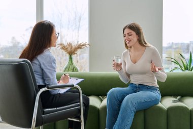 Bireysel terapi seansında kadın psikolog sosyal danışman ile konuşan genç bir kadın uzman ofisinde kanepede yan yana oturuyor. Psikoloji danışmanı zihinsel yardım desteği