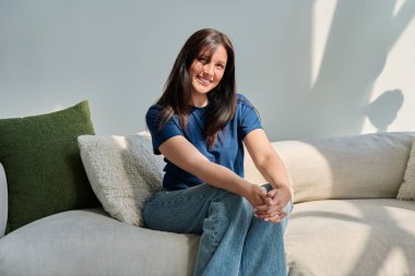 Oturma odasındaki kanepede oturan güzel esmer kadının portresi. 30 'lu yaşlarda çekici bir kadın kameraya bakıyor. Güzellik, yaşam tarzı, kadın konsepti