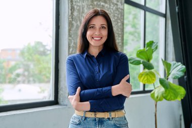 Güzel, gülümseyen, pozitif, kendine güvenen esmer kadının portresi. Pencere kenarında, çapraz kollu kameraya bakıyor. Güzellik, iş, iş, 30 'ların insanları kavramı