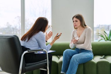 Bireysel terapi seansında kadın psikolog sosyal danışman ile konuşan genç bir kadın uzman ofisinde kanepede yan yana oturuyor. Psikoloji danışmanı zihinsel yardım desteği