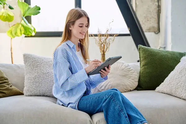 Evdeki kanepede dijital tablet kullanan genç bir kadın. Cihazlı kadın üniversite öğrencisi, rahatlama eğitimi, eğlence iletişimi eğitimi teknolojisi, yaşam tarzı gençlik konsepti