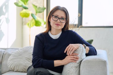 Orta yaşlı, güzel bir kadının portresi. Kanepede oturuyor. Gözlüklü, çekici, olgun bir kadın. Güzellik, sağlık, yaşam tarzı, insan kavramı