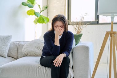 Olgun, üzgün, stresli bir kadın. Stresli, zihinsel ve fiziksel bir acı yaşıyor. Kanepede oturuyor. Sorunlar yalnızlık, baş ağrısı hormon stresi, orta yaşlı kadınların sağlığı